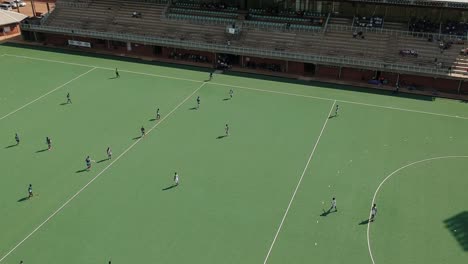 Una-Toma-De-Dron-En-Diagonal-A-La-Izquierda-De-Un-Partido-De-Hockey-Sobre-Césped-En-Condiciones-Soleadas