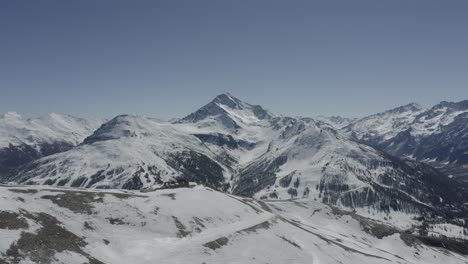 Drone-shot-flying-forwards,-over-a-ski-lift-and-showing-a-big-snowy-mountain-in-the-distant