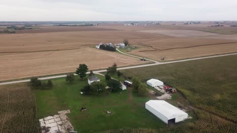 Vista-Aérea-De-Drones-En-La-Zona-Rural-De-Iowa-Con-Una-Granja-Con-Graneros-Y-Campos-De-Maíz