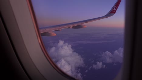 Airplane-flying-high-above-ground-with-the-sun-sunset-setting-on-the-horizon