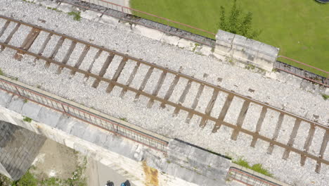 Aerial-revealing-shot-of-two-cyclists-riding-bikes-on-a-remote-country-road-with-beautiful-railway-viaduct-in-Slovenia