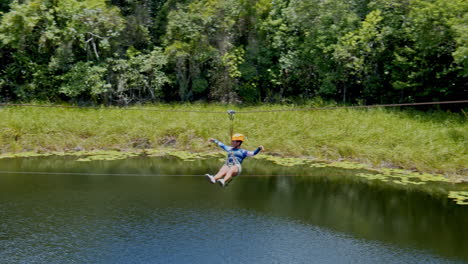 Foto-Lateral-De-Una-Chica-Haciendo-Tirolesa-Sobre-El-Estanque-En-Medio-Del-Bosque,-Cancùn,-México