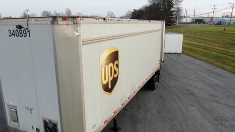 Closeup-aerial-reveals-UPS-logo-on-trailer-in-parking-lot,-express-shipping,-cargo-concept