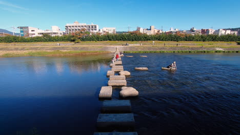 A-high-angle-shot-of-tourists-walking-on-rocky-pathway-on-Kamogawa-River-at-Kyoto,-Japan-during-afternoon-in-Autumn