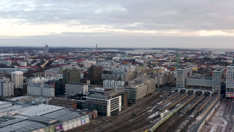 Luft-,-Schwenk--Und-Drohnenaufnahme-Mit-Blick-Auf-Die-Stadtlandschaft,-Züge-Und-Verkehr,-Die-Den-Blick-Auf-Das-Einkaufszentrum-Tripla-Und-Den-Bahnhof-Pasila-Freigibt,-An-Einem-Bewölkten-Abend-In-Helsinki,-Finnland