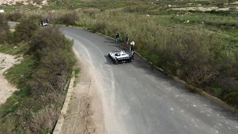 Racing-Cars-Parked-On-The-Road-Track-Between-Lush-Fields-At-The-Hill-In-Imtahleb-Malta-Before-The-Race-Starts---Aerial-Shot