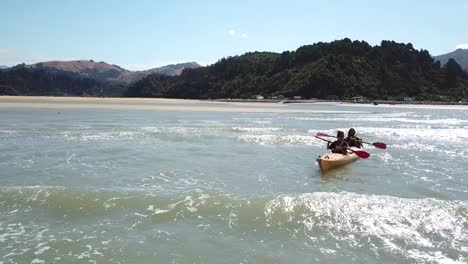 Kayaking-in-Sandy-Bay,-New-Zealand,-Orbit-Aerial-View-of-Two-People-Paddling-in-Kayak-Against-Waves