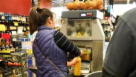 La-Mujer-Usa-Una-Máquina-De-Prensa-De-Naranja-En-La-Tienda-Para-Hacer-Jugo-De-Naranja-Fresco,-Mercado-Maduro-De-Vid