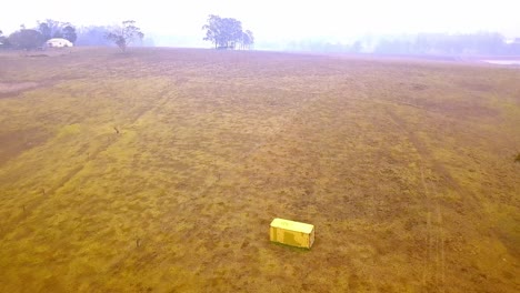 Caja-De-Remolque-Abandonada-Cerca-De-Incendios-Forestales-Con-Humo-Denso-En-La-Distancia,-Vista-Anticipada-De-Inclinación-De-Drones