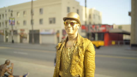 Artista-Callejero-Solitario-Pintado-En-Oro-Parado-En-El-Bulevar-De-Hollywood-Sonriendo-A-La-Cámara-En-Un-Día-Soleado-Durante-El-Brote-De-Coronavirus