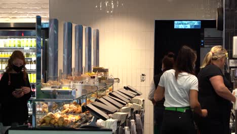 Woman-wears-a-face-mask-whilst-serving-customers-in-Kings-Cross-Station,-London,-UK