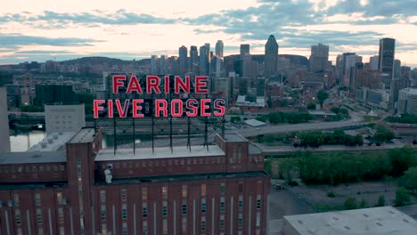 Drone-Moviéndose-Hacia-Abajo-Frente-Al-Letrero-De-Neón-Rojo-Intermitente-Del-Edificio-Farine-Cinco-Rosas-En-Montreal,-Quebec