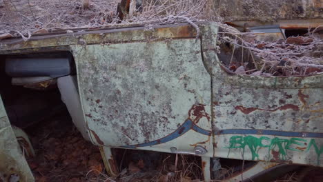 Pan-right-close-up-of-an-old-rusty-abandoned-car-embedded-in-the-ground-on-the-river-bank-of-the-Knik-river-near-Eklutna-Tailrace-area-near-Palmer-Alaska