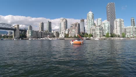 Vögel-Fliegen-über-Einen-Reflektierenden-Ozeanhafen-Von-Granville-Island,-Yaletown,-Die-Burrard-Brücke-Mit-Anlegenden-Walbeobachtungsbooten,-Ein-Vorbeifahrendes-Grillboot-An-Der-Luxuriösesten-Modernen-Architektur-Der-Türme-1-2