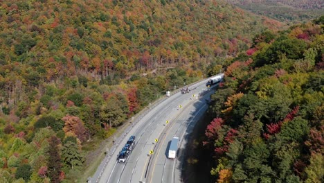 Los-Remolques-De-Tractores-Viajan-Por-La-Autopista-Interestatal-Que-Se-Curva-A-Través-Del-Terreno-Montañoso-Durante-El-Otoño,-El-Colorido-Follaje-Otoñal-Deja-Una-Escena-Acentuada