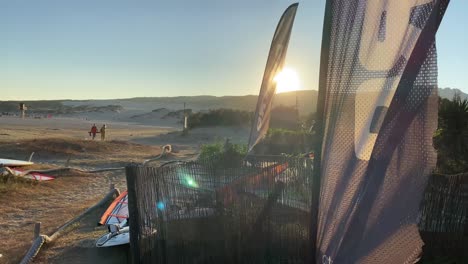 Menschen,-Die-Während-Des-Sonnenuntergangs-Am-Strand-Von-Tarifa-Spazieren-Gehen,-Mit-Vielen-Surfbrettern-Im-Sand