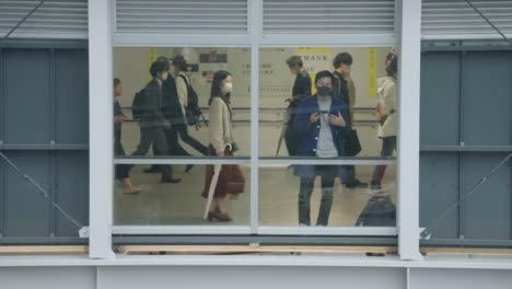 Man-Wearing-a-Masks-Talking-on-the-Phone-by-the-Window-and-People-Wearing-Masks-During-the-Pandemic