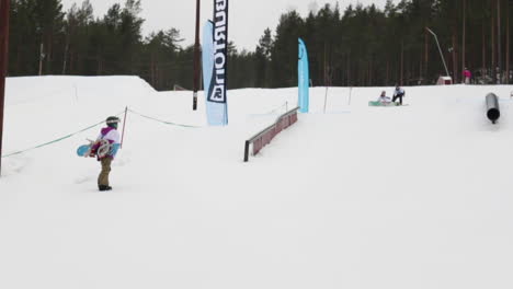 Snowboard-Mädchen-Läuft-Bei-Einem-Wettkampf-Mit-Ihrem-Snowboard-Auf-Dem-Rücken-Den-Hang-Hinauf