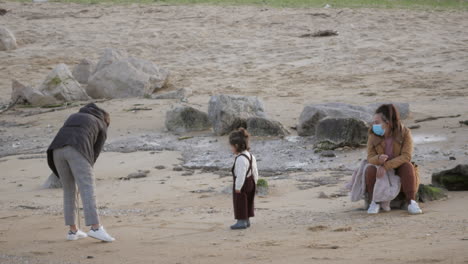 Familie-Mit-Kind,-Das-Am-Strand-Spielt-Und-Masken-Trägt