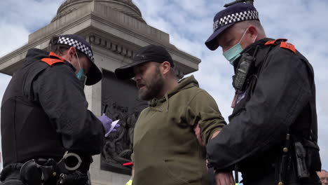 Agentes-De-Policía-Con-Máscaras-Protectoras-Detienen-Y-Registran-A-Un-Hombre-En-Busca-De-Armas-Después-De-Que-Asistiera-A-Una-Protesta-De-Conspiración-De-Coronavirus-En-Trafalgar-Square-Con-Un-Escudo-Antidisturbios