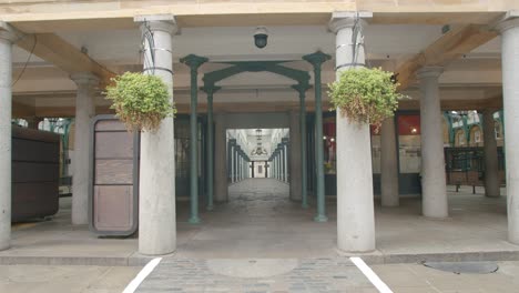 Una-Persona-Solitaria-Camina-A-Través-De-Filas-De-Tiendas-Cerradas-En-La-Plaza-Vacía-Del-Mercado-De-Covent-Garden-Con-Hermosas-Columnas-Simétricas,-Durante-La-Pandemia-De-Covid-19-De-2020