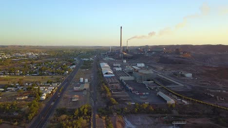 Vertically-rising-drone-footage-of-large-mining-complex-with-two-large-smoke-stacks,-one-of-which-has-smoke-coming-out