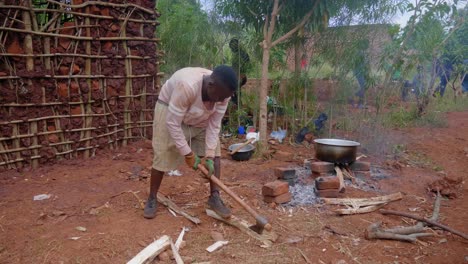 Eine-Totalaufnahme-Eines-Jungen-Afrikanischen-Mannes,-Der-In-Einem-Ländlichen-Afrikanischen-Dorf-Mit-Einer-Axt-Feuerholz-Hackt