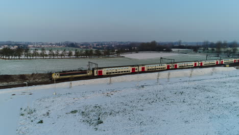 AERIAL:-A-train-riding-through-a-snowy-landscape-on-a-winter-day