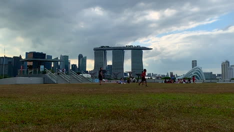 Una-Filmación-De-Un-Niño-Corriendo-Detrás-De-Una-Pelota-En-Un-Campo-Abierto-Con-El-Hotel-Marina-Bay-Sand-Singapur-En-El-Fondo