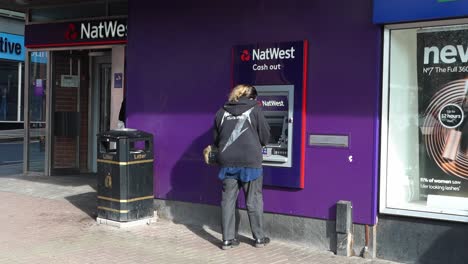 Eine-Frau-Benutzt-Einen-Natwest-Geldautomaten,-Um-Auf-Der-Hauptstraße-Im-Stadtzentrum-Geld-Abzuheben,-Bargeld-Einzuzahlen-Oder-Einige-Rechnungen-Zu-Bezahlen