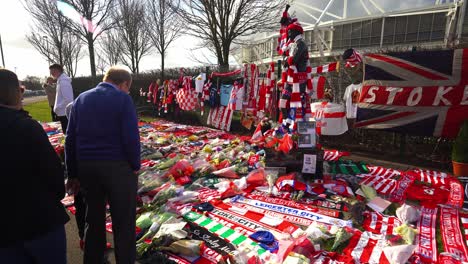 People-pay-their-respects-at-the-Gordon-Banks-statue-by-the-Stoke-City-stadium,-people-signing-shirts,-scarves,-flags-and-the-book-of-remembrance