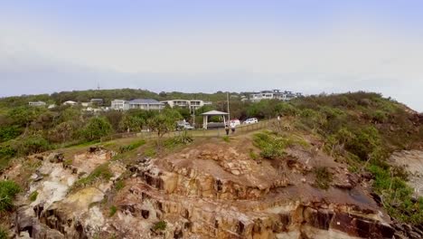 Aerial-drone-descending-shot-of-a-couple-standing-at-a-lookout-above-rocky-cliffs