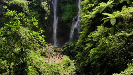 Drohnenaufnahmen-Einer-Menschenmenge,-Die-Vor-Einem-Atemberaubenden-Wasserfall-Tief-In-Einem-Grünen-Wald-Fotografiert