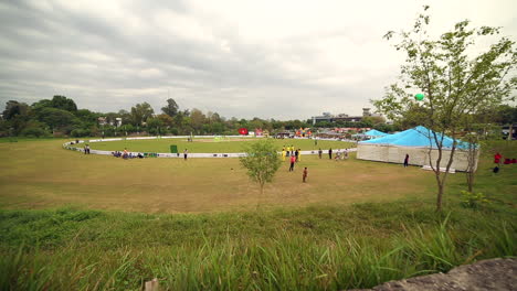 Una-Vista-Panorámica-Larga-Del-Campo-De-Deportes,-Hierba,-árboles-Y-Campamentos-Alrededor-Del-Suelo,-La-Gente-Está-Fuera-Y-Dentro-Del-Suelo