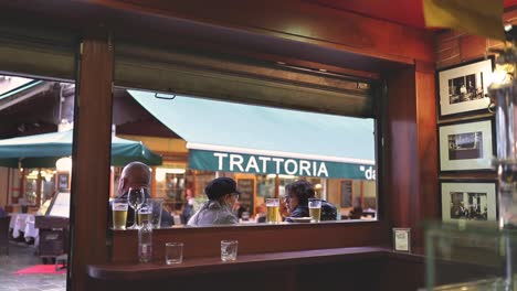 View-through-a-cafe-window-to-see-people-sitting-outside-and-walking-past-in-Venice,-Italy