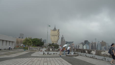 Zeitraffer-Von-Touristen,-Die-Hin-Und-Her-Gehen-Und-Das-Stadtbild-Von-Macau-Von-Der-Spitze-Des-Festungsbergs-Aus-Beobachten,-Mit-Dem-Hotel-Grand-Lisboa-Im-Hintergrund,-In-Macau-Sar,-China