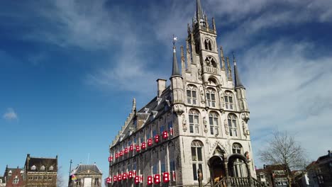 Ciudad-De-Gouda-En-Los-Países-Bajos,-Het-Oude-Stadhuys-En-El-Mercado-Con-Cielo-Azul-Y-Algunas-Personas