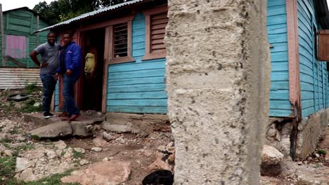 Männer-Stehen-In-Der-Tür-Eines-Heruntergekommenen-Holzhauses-In-Einem-Dominikanischen-Viertel,-Während-Kinder-Im-Hof-Stehen