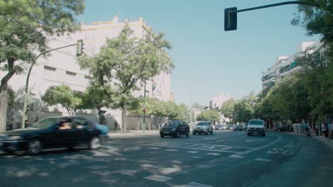 Cars-and-motorcycles-drive-on-busy-shaded-street-in-Seville,-Spain