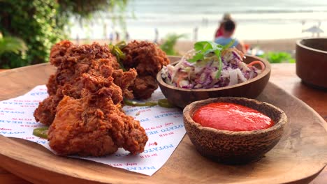 Knusprig-Frittiertes-Cricken-Mit-Scharfer-Sriracha-Suace-Und-Krautsalat-Auf-Einem-Holzschneidebrett-Mit-Meerblick,-Gefilmt-In-Bali,-Indonesien,-Urlaubsessen