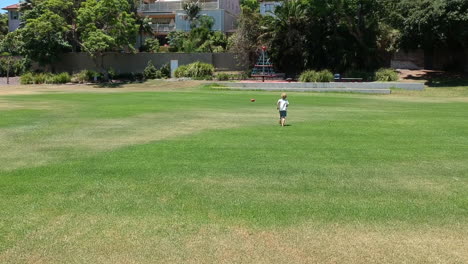 A-young-blond-boy-with-exhausting-energy-runs-across-a-large-park-and-away-from-the-camera