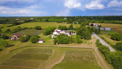 Elevación-Aérea-Sobre-Tierras-De-Cultivo-Con-Un-Arco-Iris-En-La-Distancia