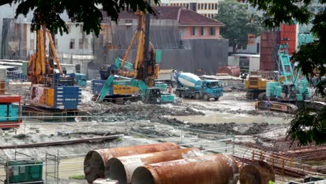 Una-Pequeña-Excavadora-Mueve-La-Pendiente-De-Cemento-En-Un-Sitio-De-Construcción-En-El-Distrito-Comercial-De-Singapur