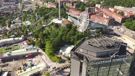 Disparo-De-Un-Dron-Contra-Un-Edificio-Con-Fachada-De-Vidrio-Y-Reflejos-Junto-A-La-Atracción-Liseberg,-Gotemburgo