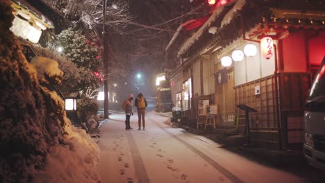 Una-Pareja-De-Pie-En-La-Calle-Durante-La-Fuerte-Nevada-En-El-Santuario-Kifune-Jinja-Por-La-Noche-En-Kyoto,-Japón