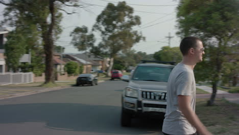 Panning-shot-of-young-man-looking-both-ways-then-walks-across-street-in-the-late-afternoon