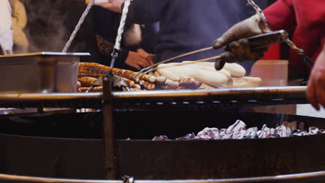 Close-up-view-of-outdoor-charcoal-grill-and-man-turning-bratwurst-and-other-food-as-it-cooks