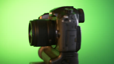 Mirrorless-camera-spins-around-through-frame,-in-front-of-green-studio-back-drop