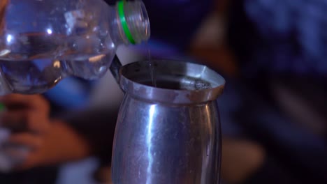 Close-up-pours-water-from-a-bottle-into-the-pot,-Tilt-down-to-fire-under-the-pot