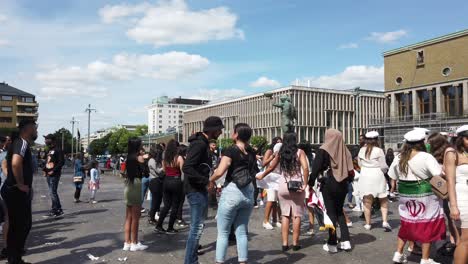 Group-of-young-people-dancing-on-street-waving-Middle-Eastern-flags,-panning-shot